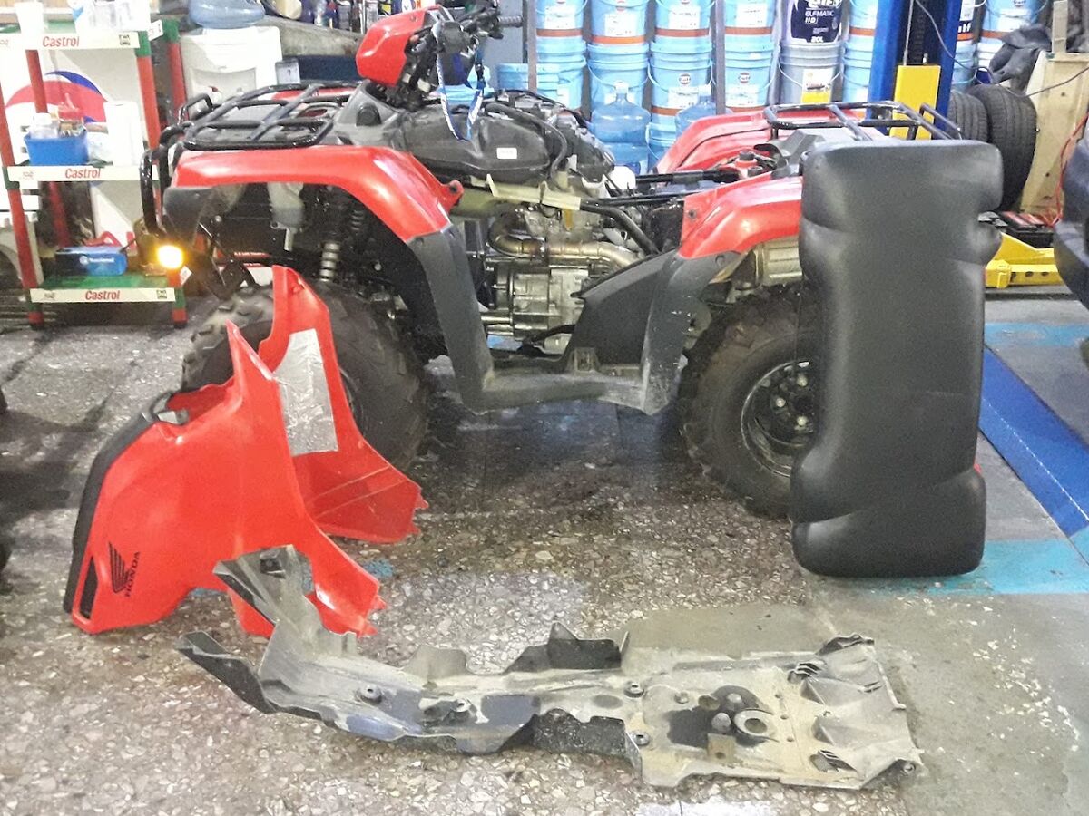 Cuatriciclo Honda desarmado en el taller para un service, con los plásticos y la protección inferior a un costado
